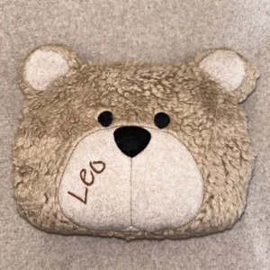 Wärmekissen Bär personalisiert aus Baumwollplüsch in braun. Das Wärmekissen besteht aus dem Bärenkopf, mit abstehenden Ohren, aufgenähten schwarzen Augen und brauner Nase. Der Name Leo wurde in die Schnauze gut leserlich in 3 cm großen Buchstaben auf der linken Seite eingestickt.